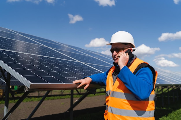 Male engineer in hardhat standing near solar panels and talking on the phone