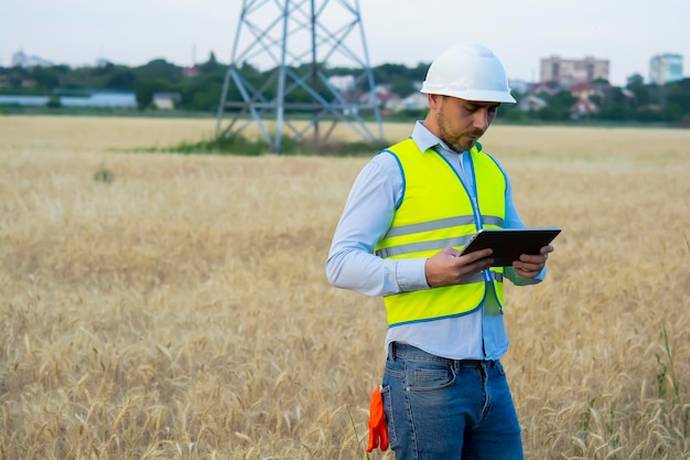 Male engineer in a helmet and goggles uses a smartphone for field work near a telecommunications tow