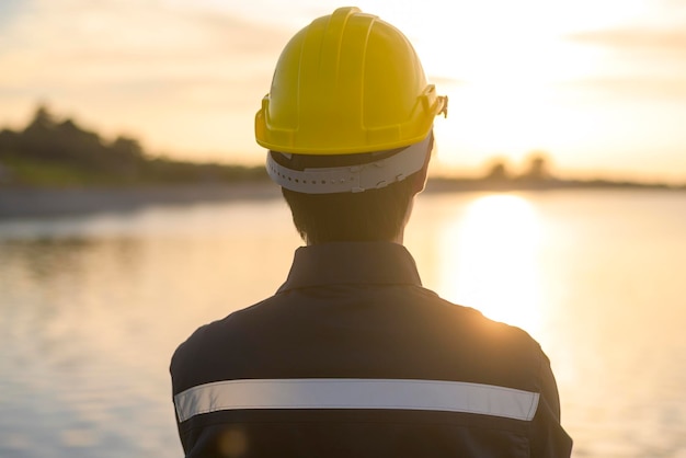 A male engineer wearing a protective helmet at sunset.