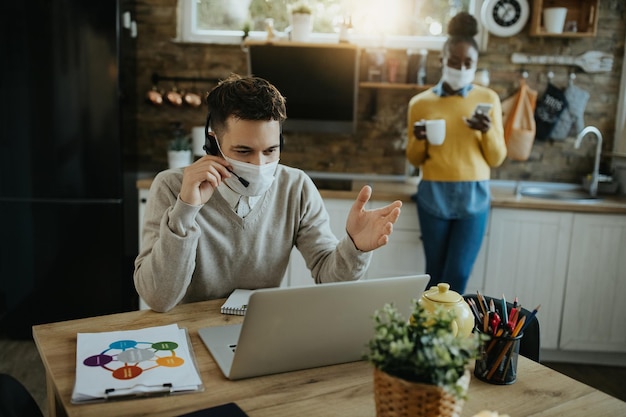 Male entrepreneur with face mask talking during conference call at home