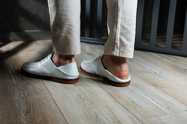 Male feet closeup in white casual shoes Fashionable young man standing in leather stylish white moccasins in trousers Seasonal summer men's shoes Casual street style