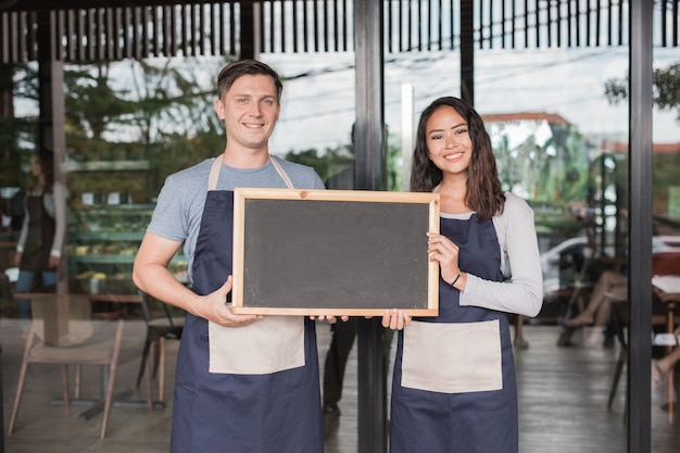 Male and female cafe owner proudly standing in front of their cafe or coffee shop