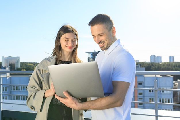 Male and female colleagues with laptop standing on the roof