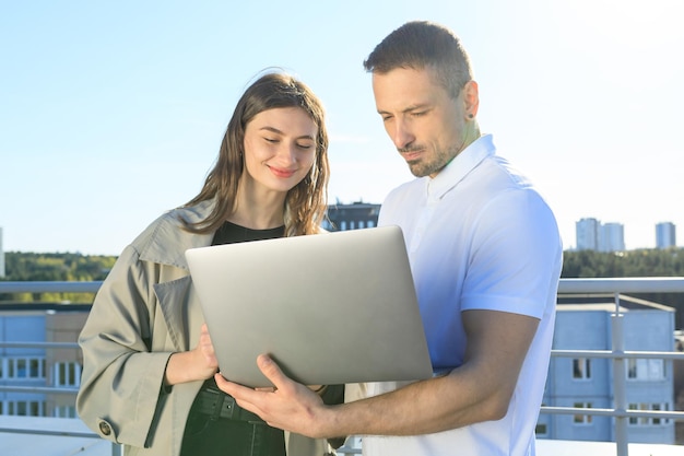 Male and female colleagues with laptop standing on the roof