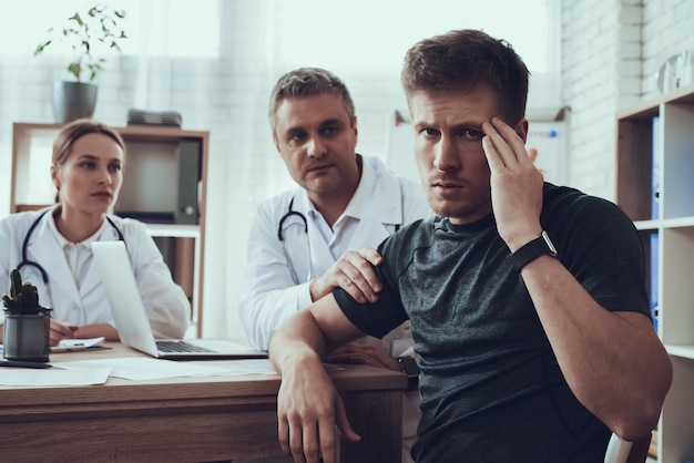 Male and female doctors at table in office. Athlete's head hurts.