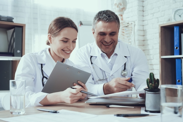 Male and female doctors with stethoscopes at table in office. Doctors are comparing notes.