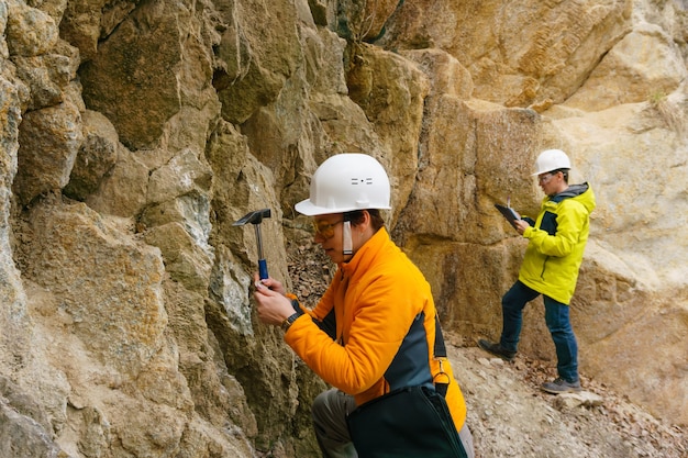 Male and female geologists takes a sample of the mineral and record data in a canyon