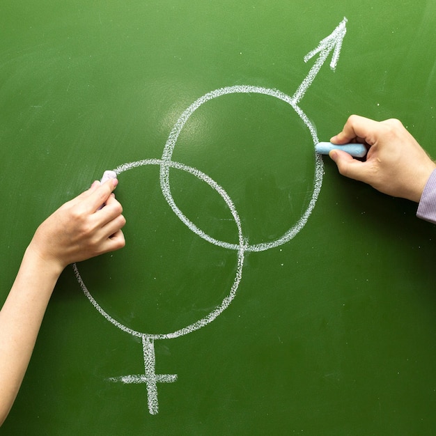 Male and female hands draw symbols of the masculine feminine principle with chalk on the blackboard. The concept of love at school