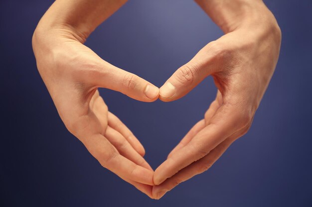 Male and female hands making heart with fingers on blue background