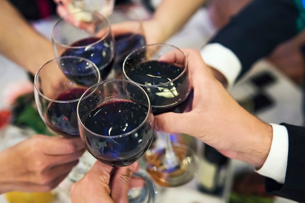 Photo male and female hands with filled glasses of red wine above the restaurant tabletop. drinking toasts and clinking tumblers at a formal dinner party. drinking wine at a banquet. in full swing of feast.