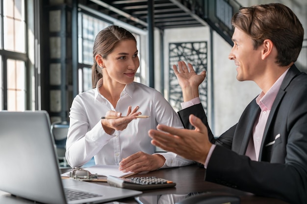 Male and female office managers smiling discussing work man in black suit and woman in white shirt Smiling business partners in office room sitting to table with laptop concept of work