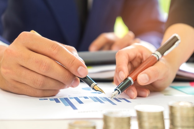 Male and female office workers use a pen in their hands pointing at the graph