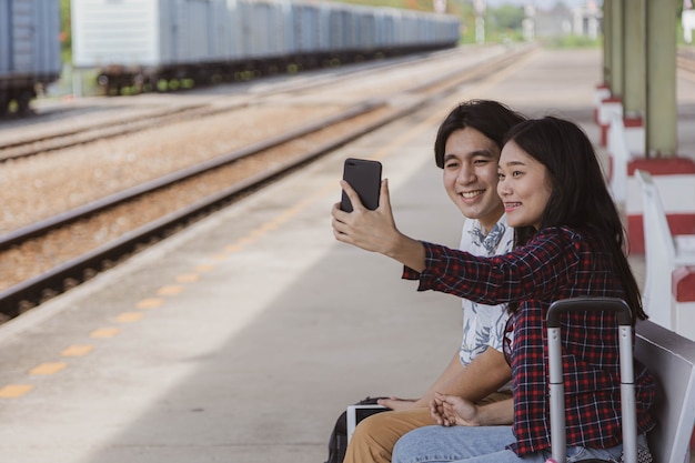 Male and female tourists are using their phones to take a selfie at the train station.