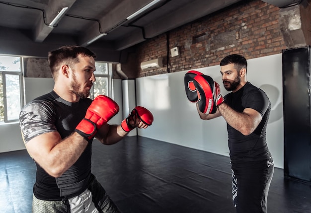 Photo male fighter trains punches with partner with training boxing paws