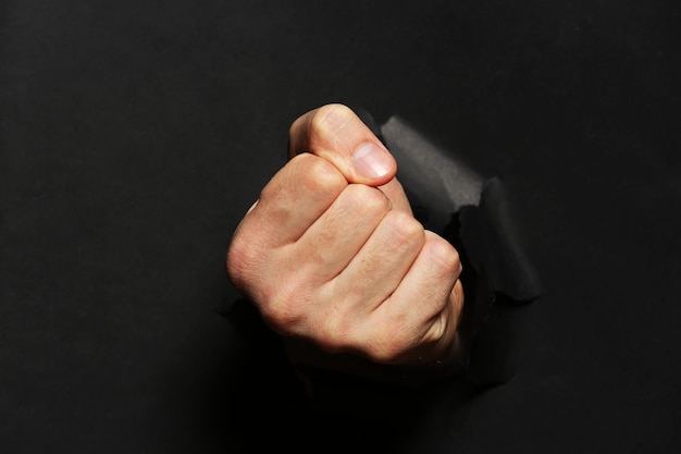 Male fist punching through black paper