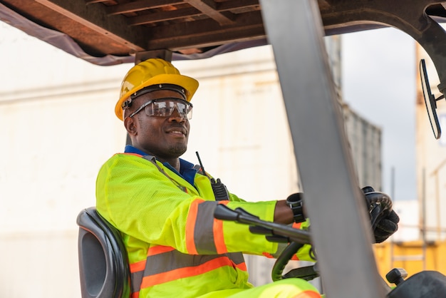 Male foreman wear safety glasses and yellow helmet driving a forklift at Cargo container shipping