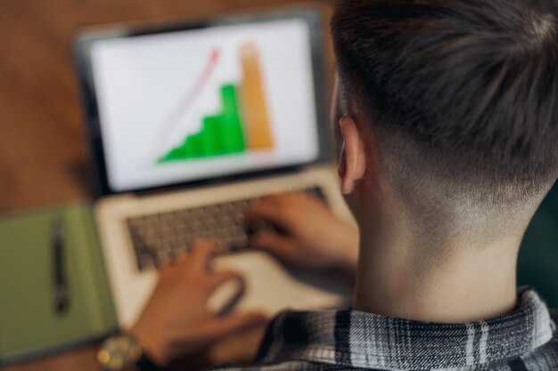 male freelancer analyzing chart on laptop while typing on keyboard and working on business project