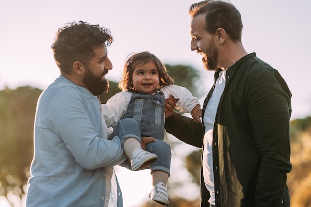 Male gay couple holding their young daughter up in the air Modern family concept