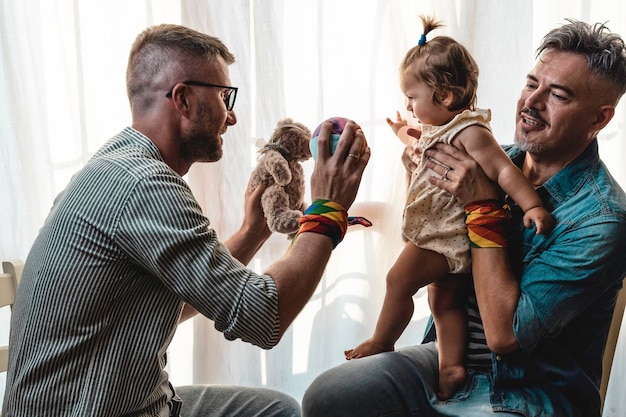 Male gay couple with adopted baby girl at home Two handsome fathers playing with their daughter Lgbtq family at home Diversity concept and LGBTQ family relationship