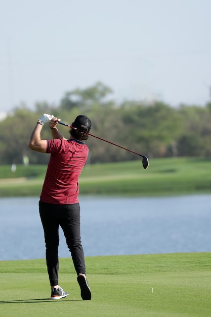 Male golf player wearing red shirt hitting ball