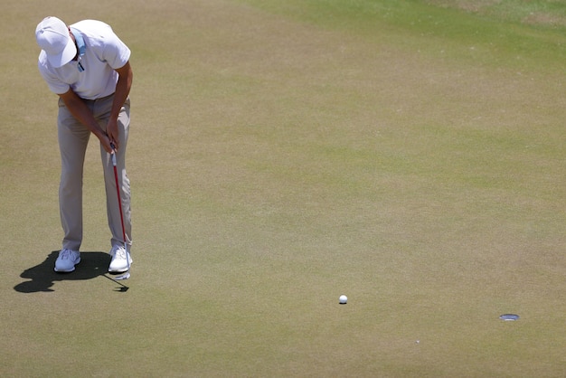 Male golf player wearing white shirt putting on sunny day