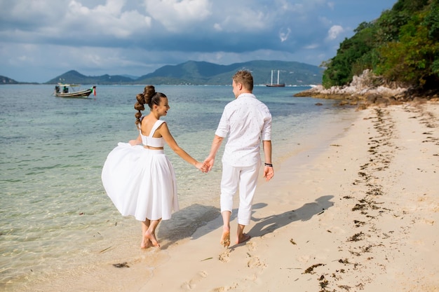 Male groom and female bride walking barefoot on beach