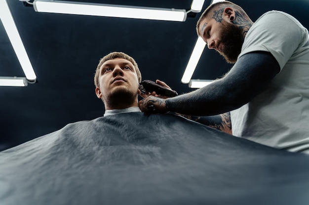 Male haircut with electric razor Tattooed Barber makes haircut for client at the barber shop by using hairclipper Man hairdressing with electric shaver Bottom view