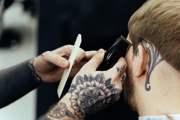 Male haircut with electric razor Tattooed Barber makes haircut for client at the barber shop by using hairclipper Man hairdressing with electric shaver