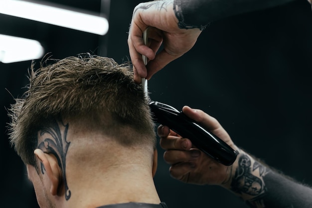 Male haircut with electric razor Tattooed Barber makes haircut for client at the barber shop by using hairclipper Man hairdressing with electric shaver