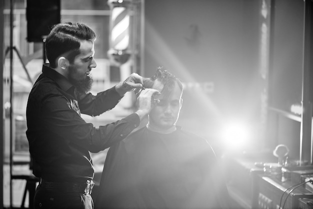 Male hairdresser cuts client with scissors in the barbershop black-and-white photo