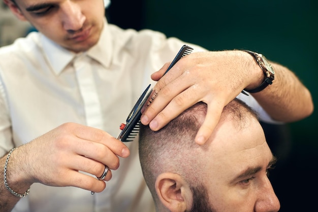 Male hairdresser making short haircut for client in modern barbershop Concept of traditional haircutting with scissors