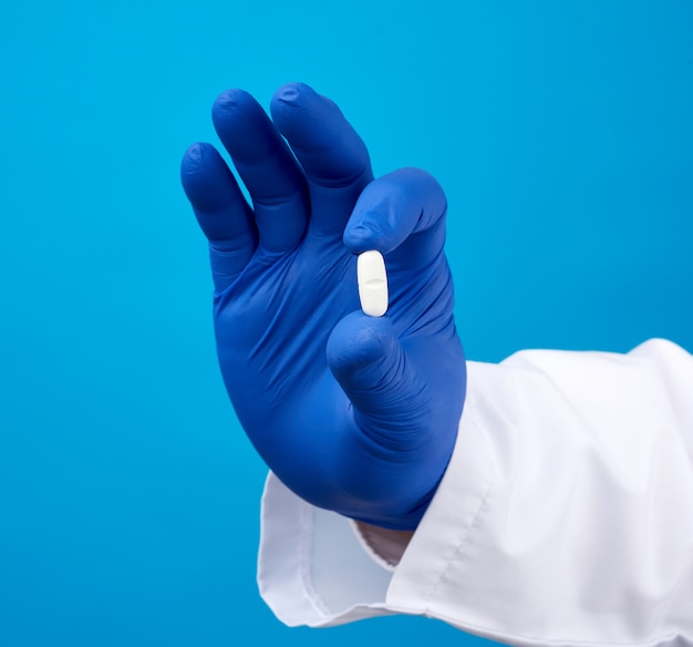 Photo male hand in blue sterile gloves holds an oval white pill, medical treatment concept for diseases