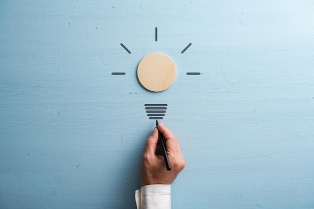 Male hand drawing a light bulb stem with black marker to a bulb made of wooden cut circle