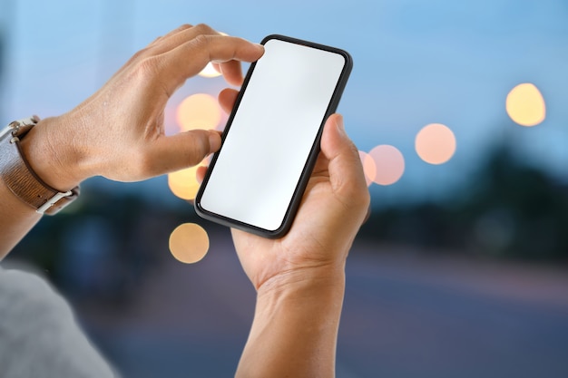 Male hand holding blank screen mobile smart phone at street night.