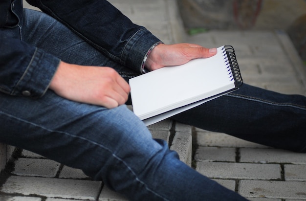 Male hand holding a book and sitting outside