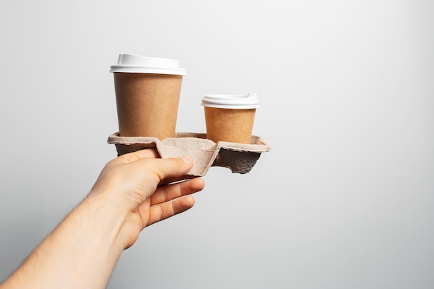 Male hand holding cardboard holder with two paper cups of coffee takeaway