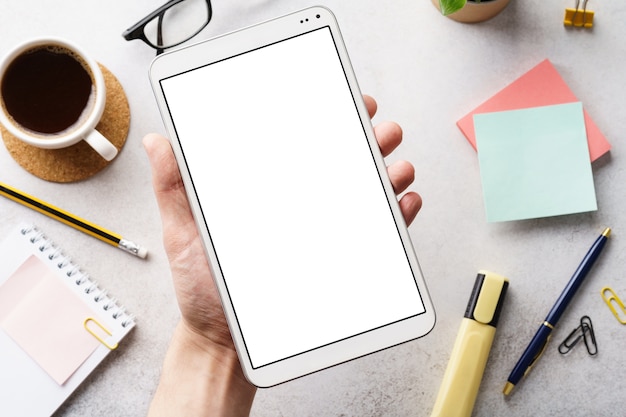 Male hand holding a device with white blank screen over a desk.