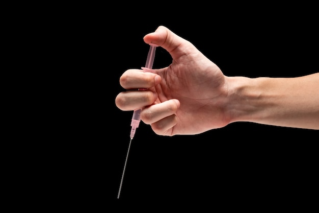 Male hand holding medical tool syringe on a black background.