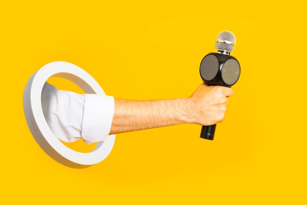 Male hand holding a microphone in a white ring on a yellow background