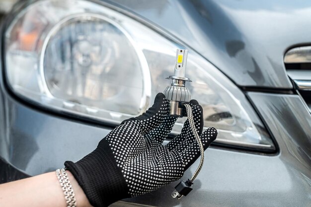 Male hand holding modern LED h7 bukb near headlamp of a car