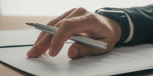 Male hand holding a pen resting on a business contract