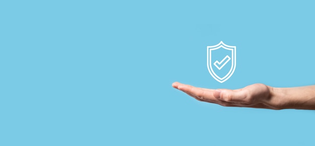 Male hand holding protect shield with a check mark icon on blue background. Protection network security computer and safe your data concept .