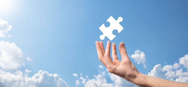 Male hand holding puzzle icon on blue background. pieces representing the merging of two companies or joint venture, partnership, Mergers and acquisition concept.