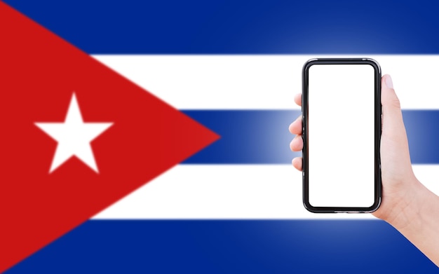 Male hand holding smartphone with blank on screen on background of blurred flag of Cuba Closeup view