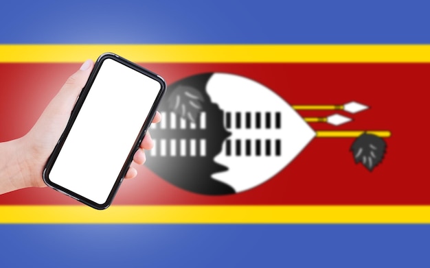 Male hand holding smartphone with blank on screen on background of blurred flag of Eswatini Closeup view