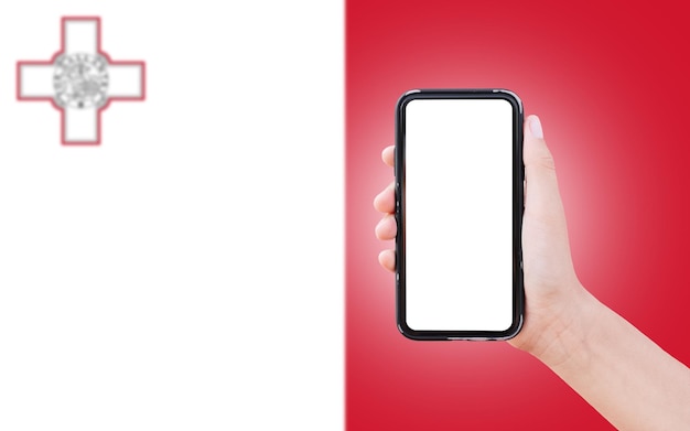 Male hand holding smartphone with blank on screen on background of blurred flag of Malta Closeup view