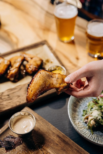 Male hand holding spicy grilled bbq chicken wings and eating with beer in pub