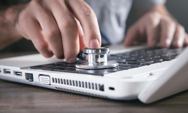 Male hand holding stethoscope on a laptop keyboard.