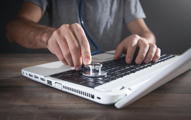 Male hand holding stethoscope on a laptop keyboard