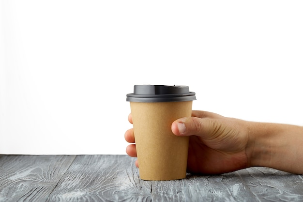 Male hand holding a take away coffee paper cup on grey wooden background